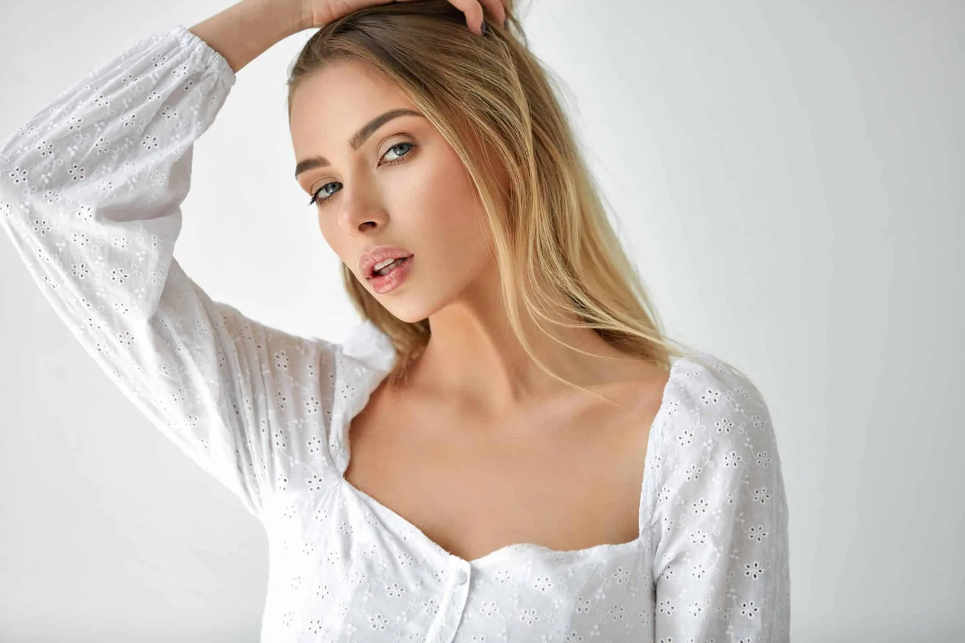 Young woman with long blonde hair in a white eyelet embroidered top, looking directly at the viewer