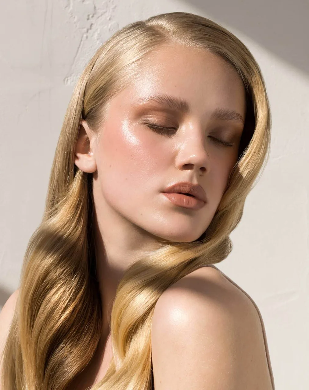 Young woman with closed eyes, natural glowing skin, and long blonde wavy hair