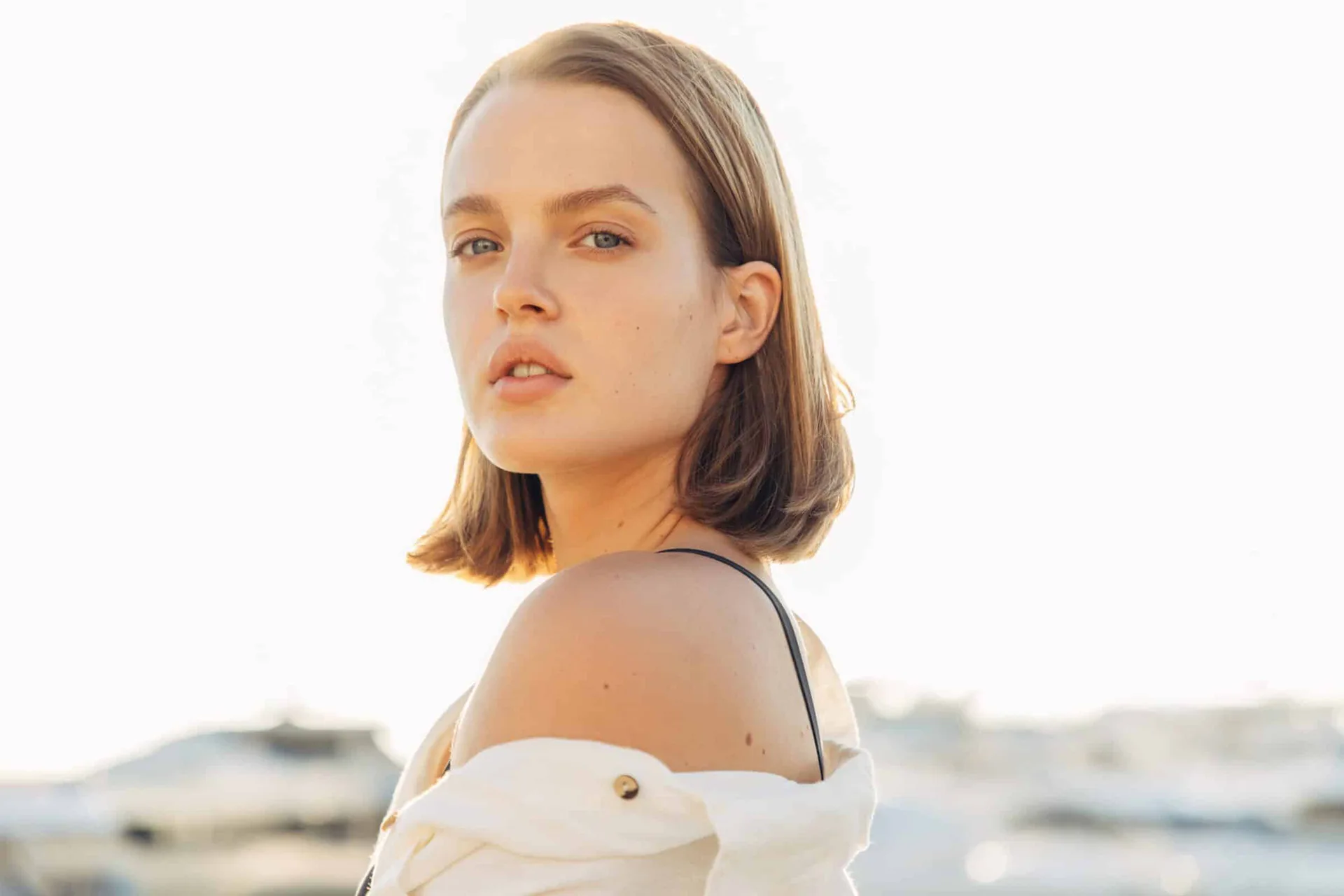 A young woman with a bob haircut looks directly at the camera, bathed in warm natural light