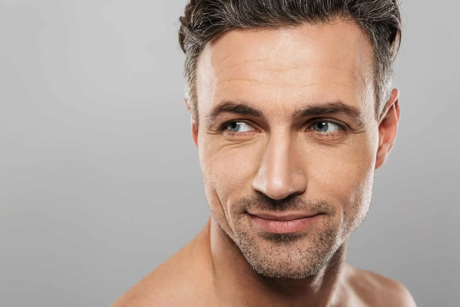 A handsome middle-aged man with blue eyes and salt-and-pepper hair looks right with a faint smile. He has a slight stubble